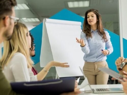 Confident young team leader giving a presentation to a group of young colleagues as they sit grouped by the flip chart in the small startup office